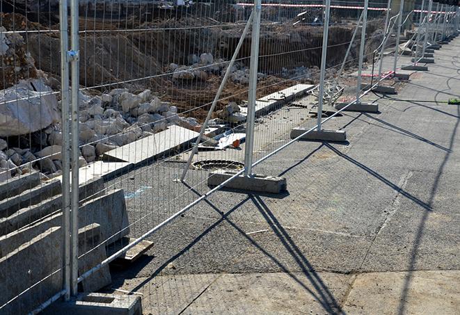 workers constructing a temporary fence with metal panels and braces at a work area